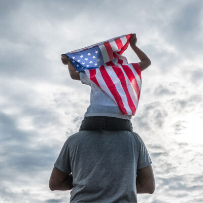 Child holding American flag sitting on dad's shoulders