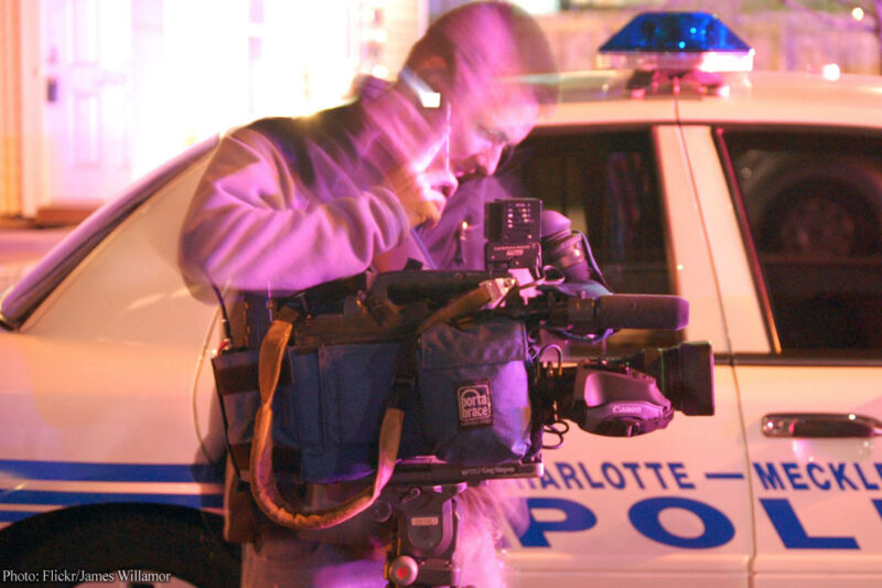 Reporter in front of police car at police activity scene