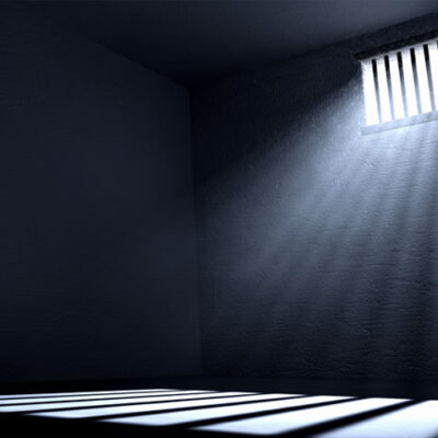 Light streaming through a barred window casts a shadow of the bars the floor of a prison cell