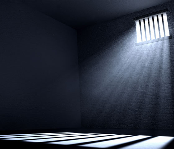 Light streaming through a barred window casts a shadow of the bars the floor of a prison cell