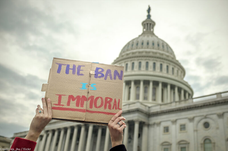 Person holding "The Ban Is Immoral" sign in front of Capitol building