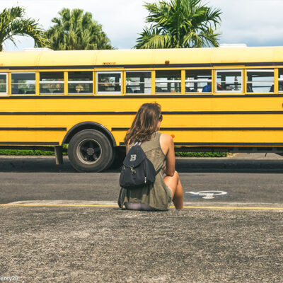 Girl sitting outside with school bus
