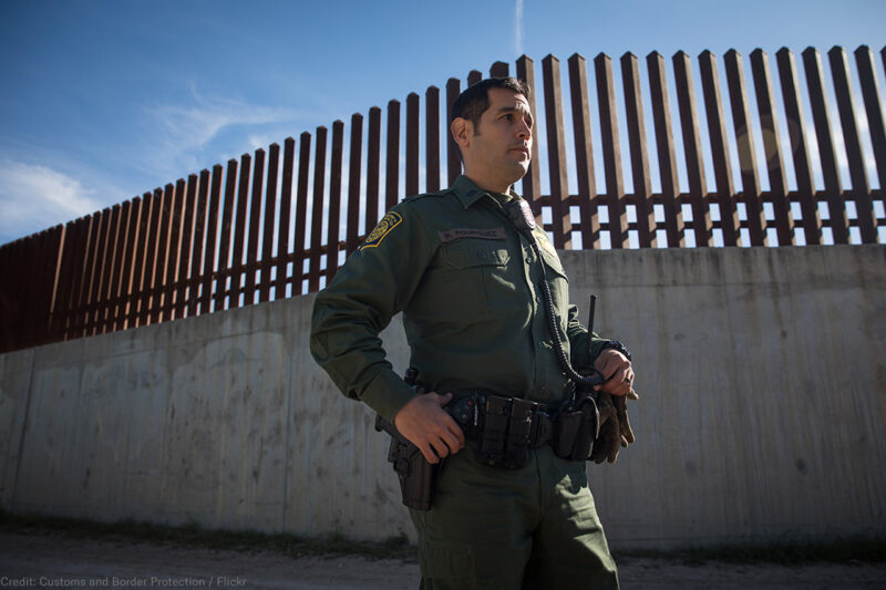 CBP Agent standing before southern border wall.