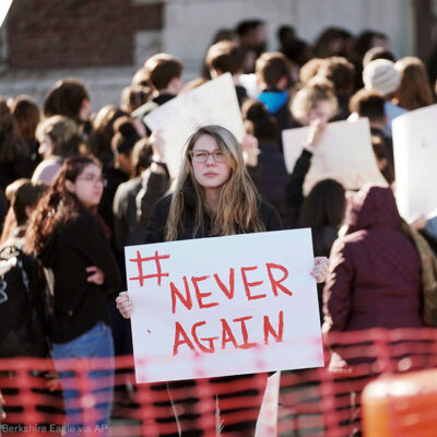 Student protester holding "#Never Again" sign at rally