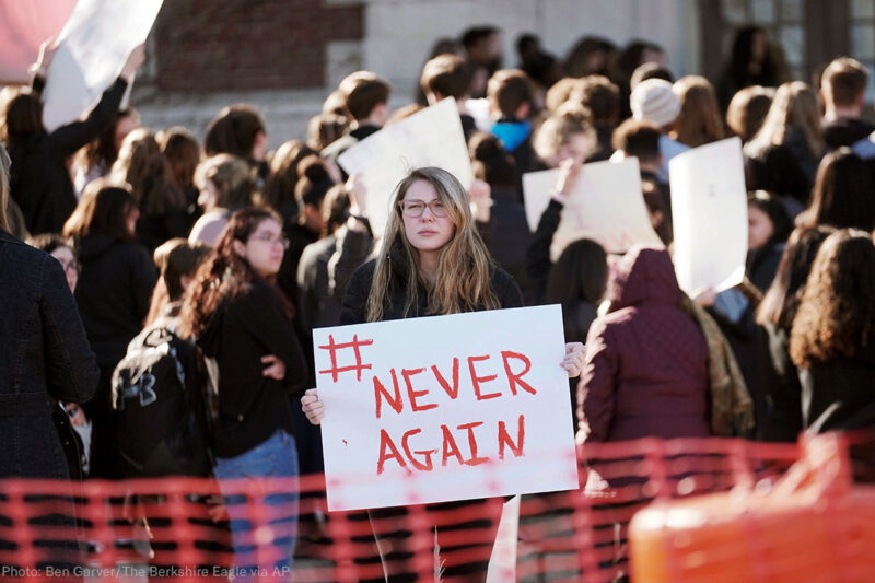 Student protester holding "#Never Again" sign at rally