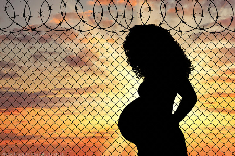 Silhouette of a pregnant woman standing near a fence with barbed wire