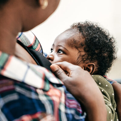 A Black person chest-feeding an infant