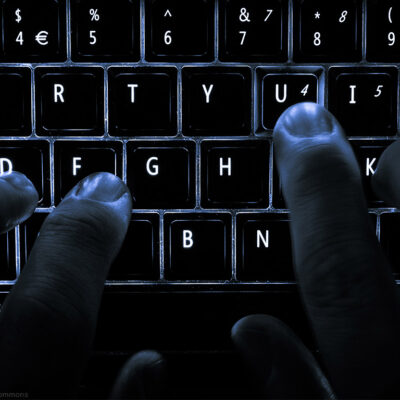 A backlit laptop computer keyboard. Most fingers are on the "home" keys for touch-typing; the 'U' key is being pressed.