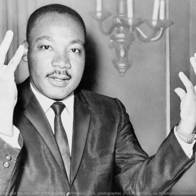 Rev. Martin Luther King, head-and-shoulders portrait, seated, facing front, hands extended upward, during a press conference