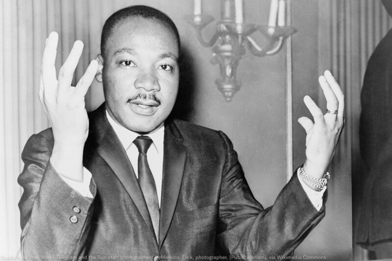 Rev. Martin Luther King, head-and-shoulders portrait, seated, facing front, hands extended upward, during a press conference