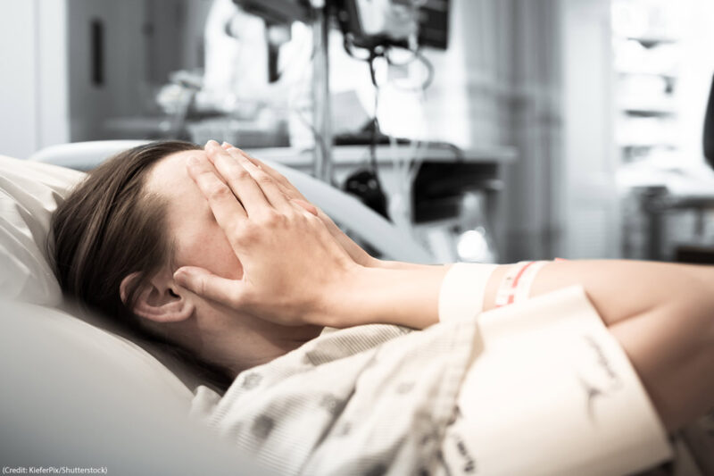 Image of a woman in a hospital bed covering her eyes