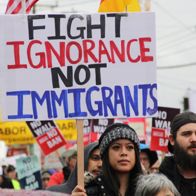 A protester holding a sign with the text "fight ignorance not immigrants"