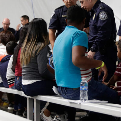 Migrants seated in a processing area at a tent courtroom