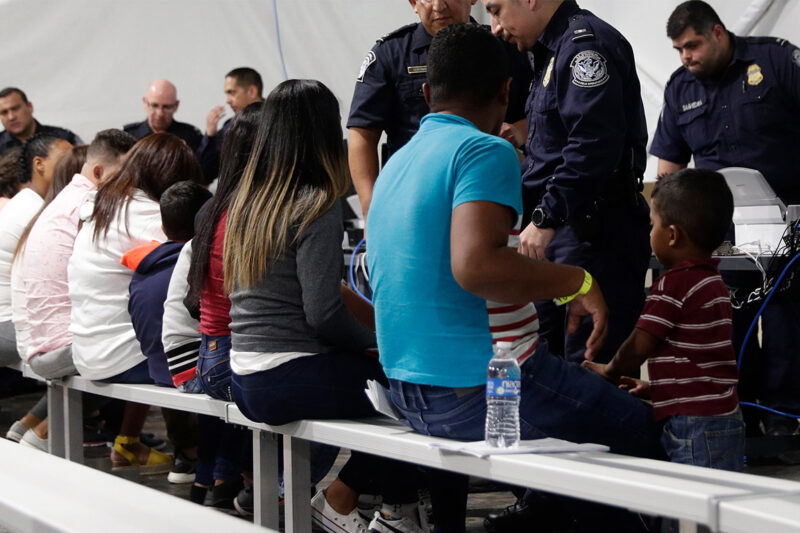 Migrants seated in a processing area at a tent courtroom