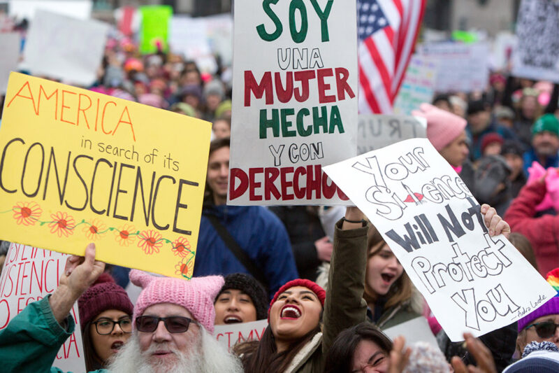 A crowd of people at a protest hold signs in english and spanish