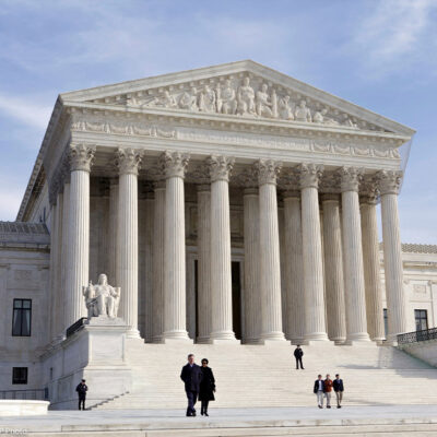 The front of the Supreme Court, as a few people are walking up and down its stairs, on a sunny day in 2012.