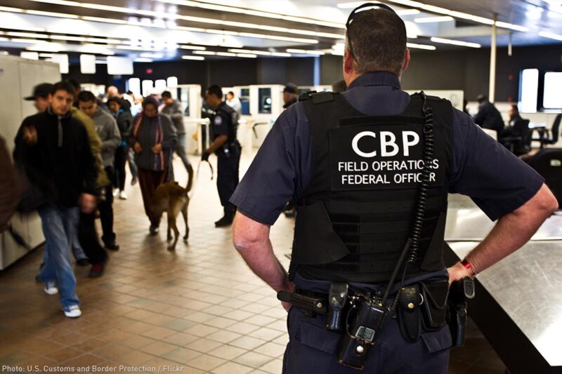 A CBP officer watches over travellers at an airport.