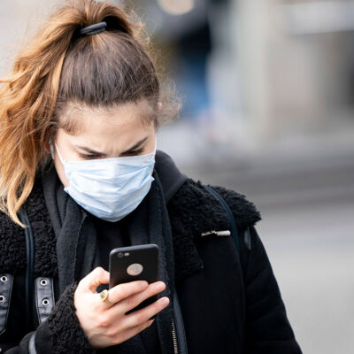 A woman wearing a mask looks at her smartphone.