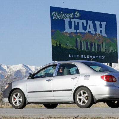 A silver car drives past the "Welcome to Utah" sign at the state border.