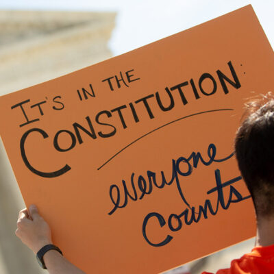 A demonstrator holding a sign with the text "It's in the Constitution: everyone counts" outside the Supreme Court.