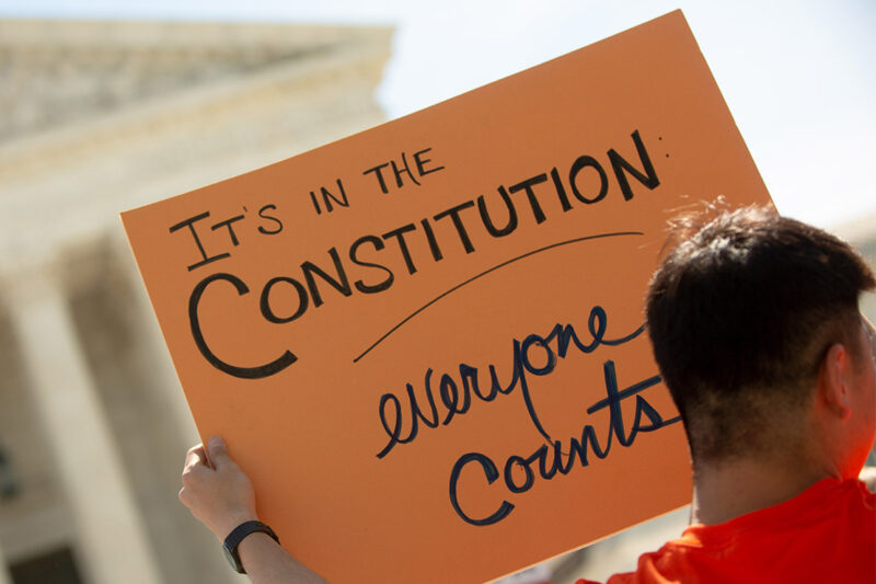 A demonstrator holding a sign with the text "It's in the Constitution: everyone counts" outside the Supreme Court.