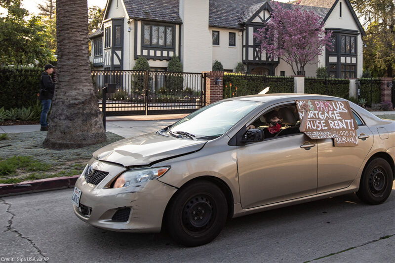 A protestor drives by L.A. Mayor Eric Garcetti's mansion with a sign in favor of extended rent and mortgage protections.