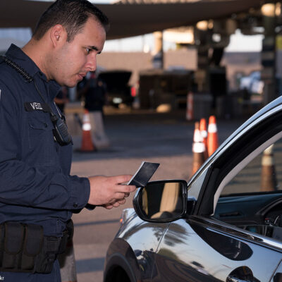 A U.S. Customs and Border Protection checking the identification of someone seated in a car.