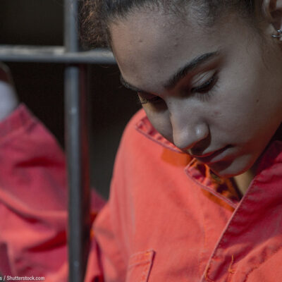 A incarcerated woman standing behind bars.