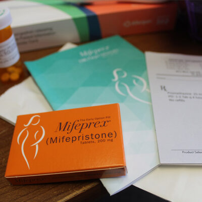 A desk with a box of Mifepristone, an information pamphlet, and a doctor's prescription pad.