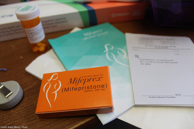 A desk with a box of Mifepristone, an information pamphlet, and a doctor's prescription pad.