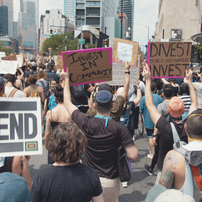 Protesters marching in a demonstration with signs calling on officials to divest from police and invest in communities.