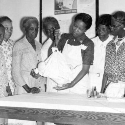 A black nurse showing black midwives how to use a portable scale to weigh babies.