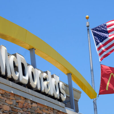 McDonalds logo besides the company flag and the American flag on a flagpole outside of the restaurant chain.