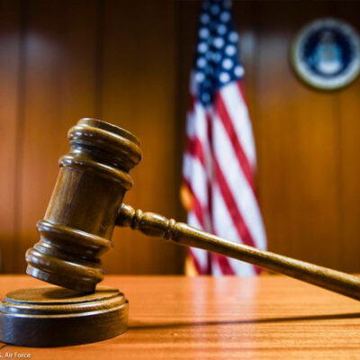 A gavel rests on the judge’s bench in a courtroom with American flag in the background.