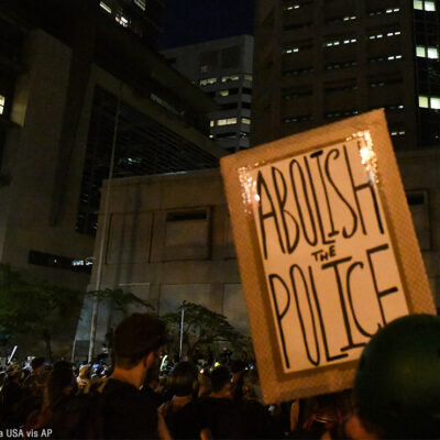 A group of protesters with one holding a sign with the text, "Abolish the Police."