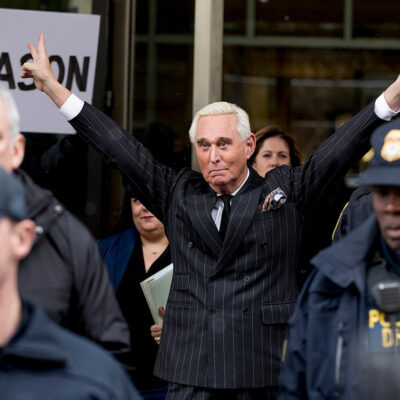 Roger Stone leaving federal court with raised arms wide and flashing two V-shaped hand signs.