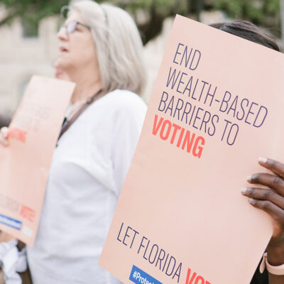 Woman holding sign reading 'End wealth based barriers to voting"