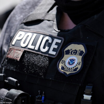 A close up of a police officer wears a "Police" label beside a U.S. ICE (standing for Immigration and Customs Enforcement) badge on his vest.
