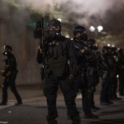 Police in Portland wear riot gear and armed with guns as smoke fills the streets.
