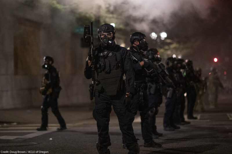 Police in Portland wear riot gear and armed with guns as smoke fills the streets.