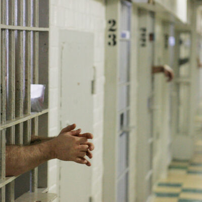 Prisoners reach through the metal bars of their cells.