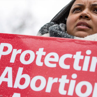 A woman holds a "protecting abortion access" sign in the rain.