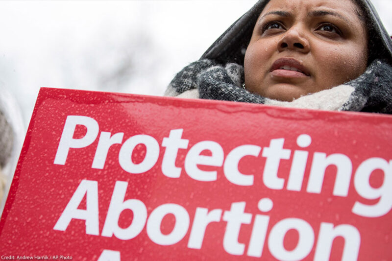 A woman holds a "protecting abortion access" sign in the rain.