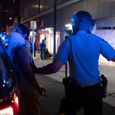 A police officer holds a man against the back of his police car during a night of unrest in downtown Minneapolis.