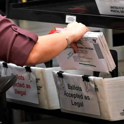An election worker sorts vote-by-mail ballots in bins.