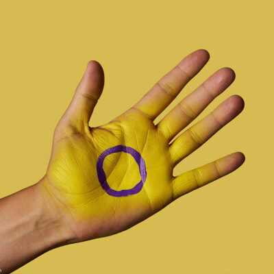 A closeup of the intersex flag painted on the palm of a person's hand.