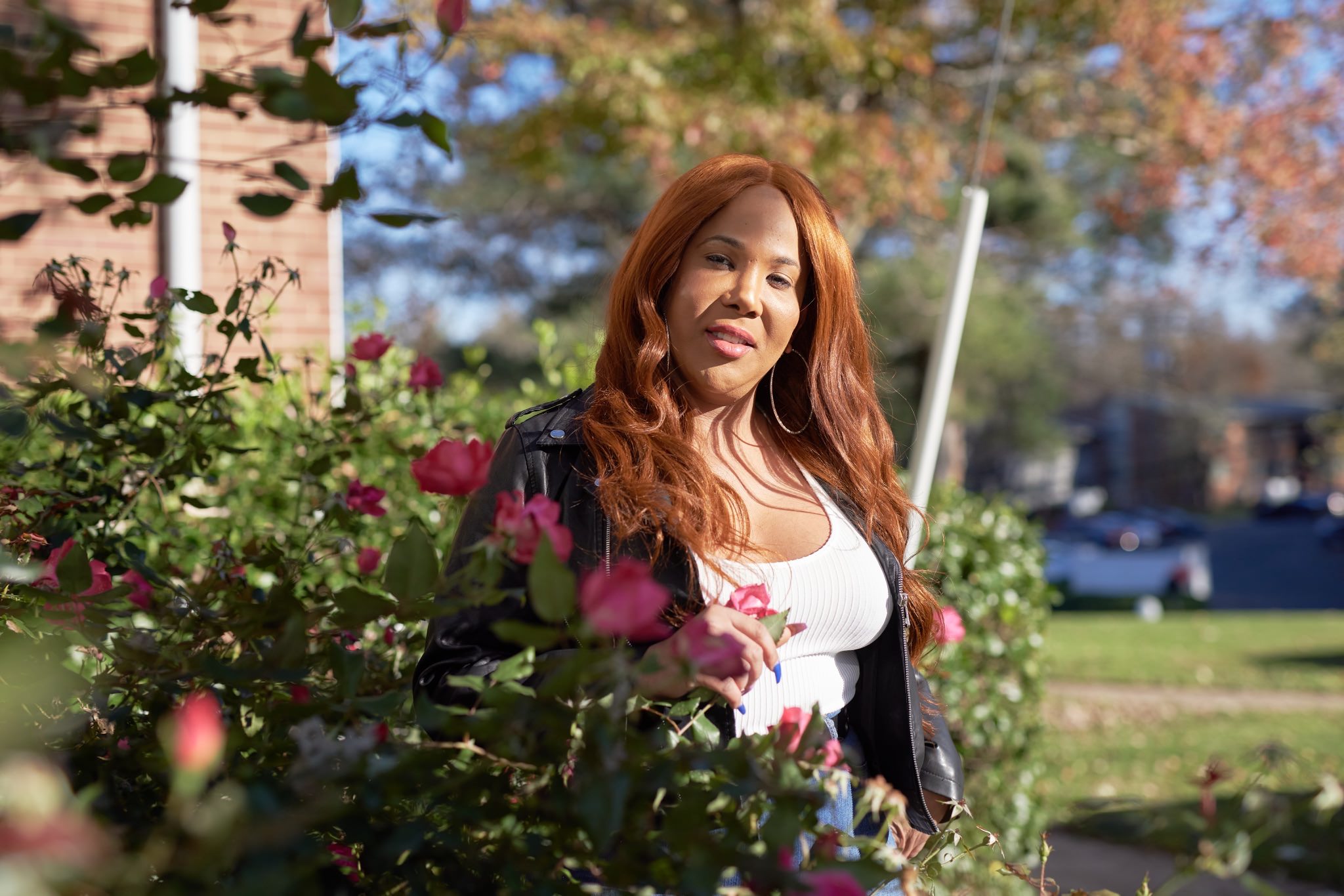 Black trans woman wearing a leather jacket standing in a garden with flowers