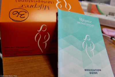 An orange Mifepristone box and blue medication guide.