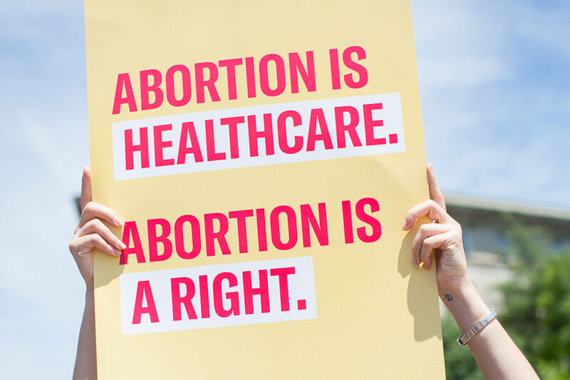 Two hands holding a sign with the text "Abortion is healthcare. Abortion is a right."