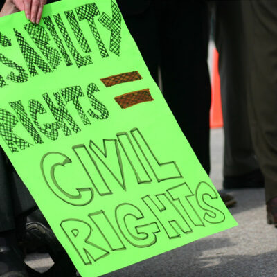 A wheelchair user holding a sign with the text "Disability rights = civil rights."